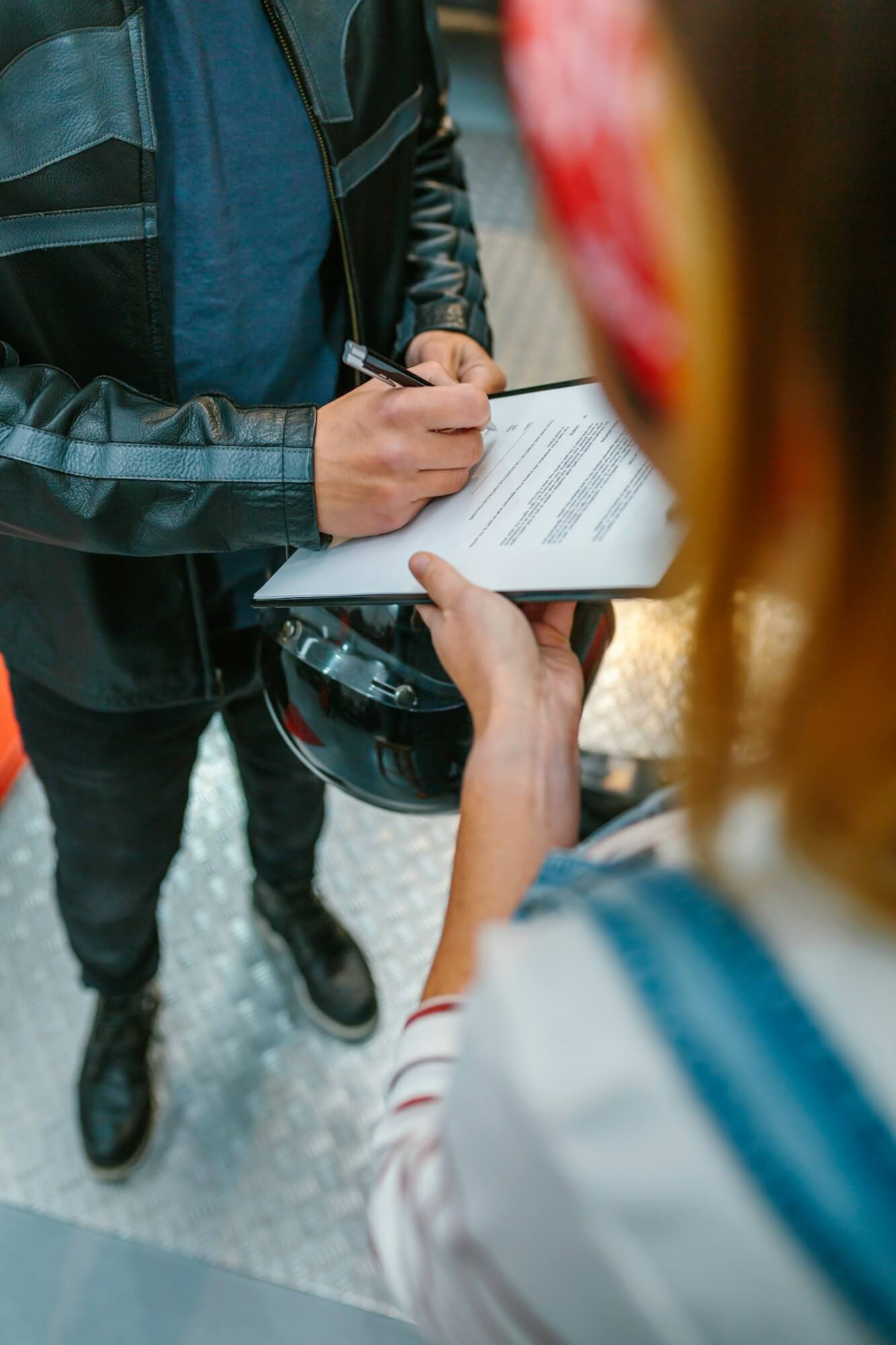 Biker man signing insurance policy on workshop while female mechanic holding clipboard