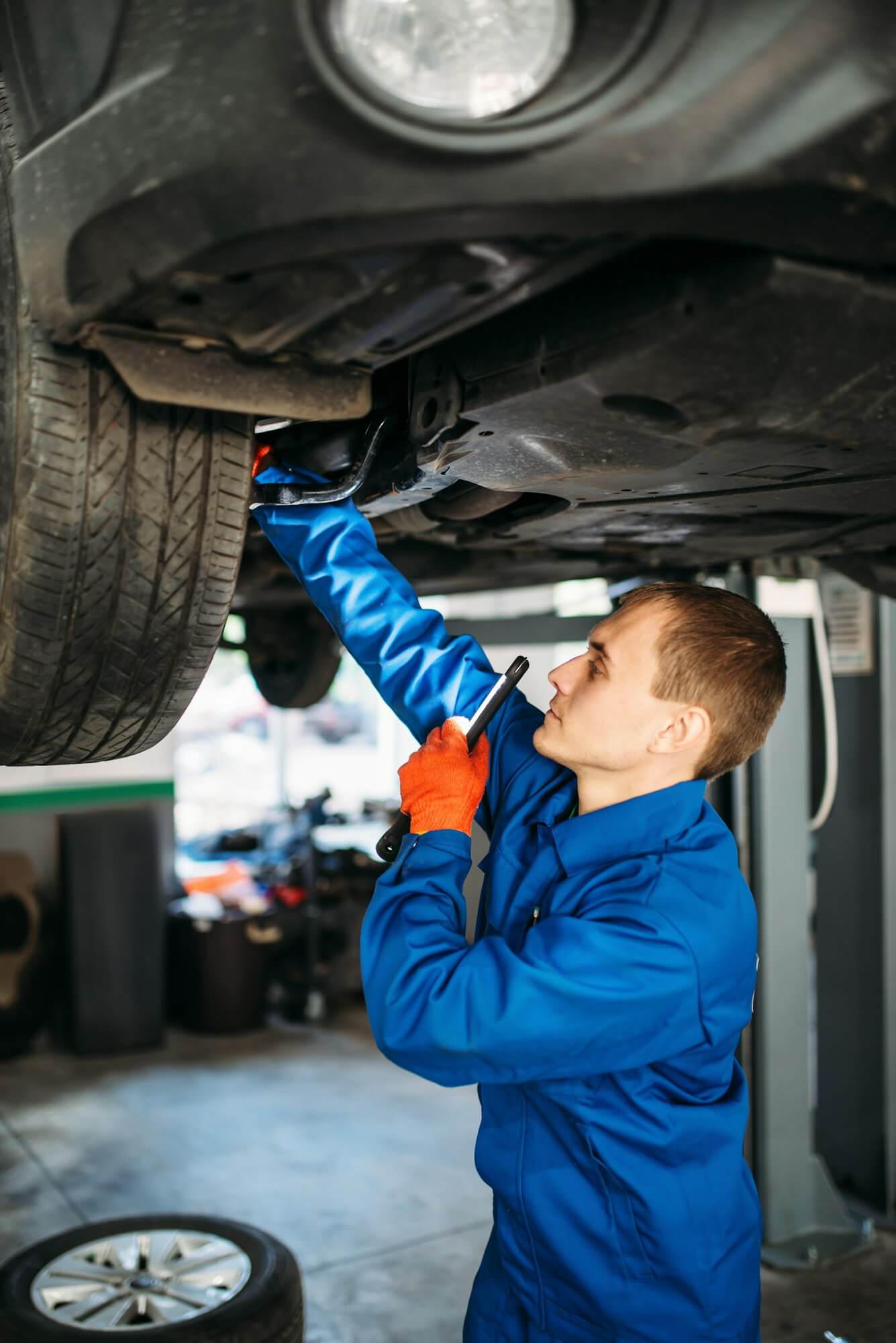 Mechanic with lamp checks the car suspension